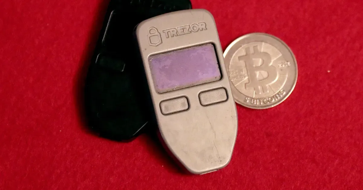 Two Trezor One hardware wallets next to a physical bitcoin coin
