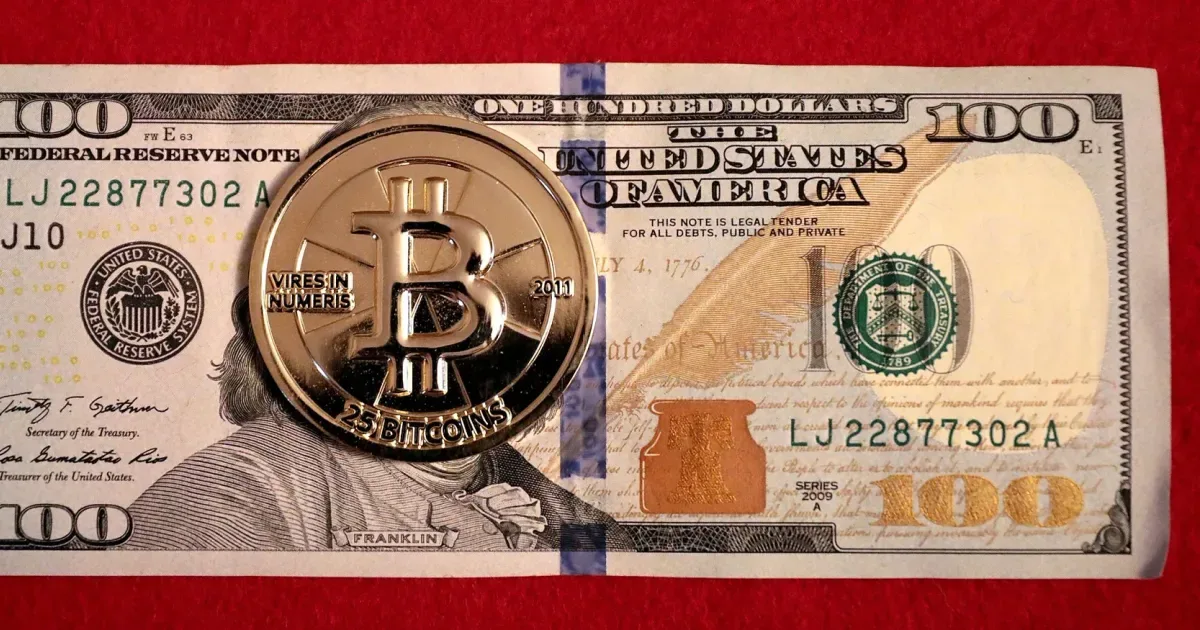 A physical Casascius bitcoin coin resting on a $100 bill