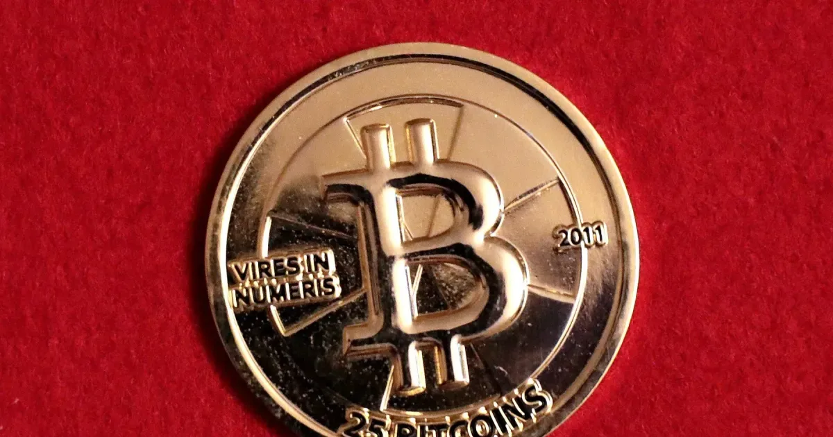A physical 25 BTC gold Casascius coin on a red background